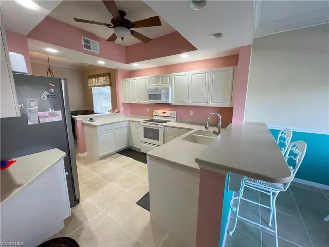 Kitchen featuring sink, white appliances, a breakfast bar, white cabinetry, and kitchen peninsula