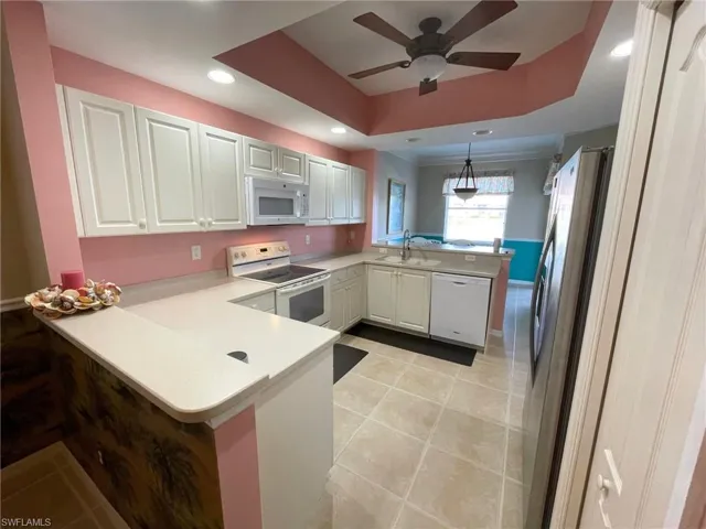 Kitchen with kitchen peninsula, white cabinetry, hanging light fixtures, a tray ceiling, and white appliances