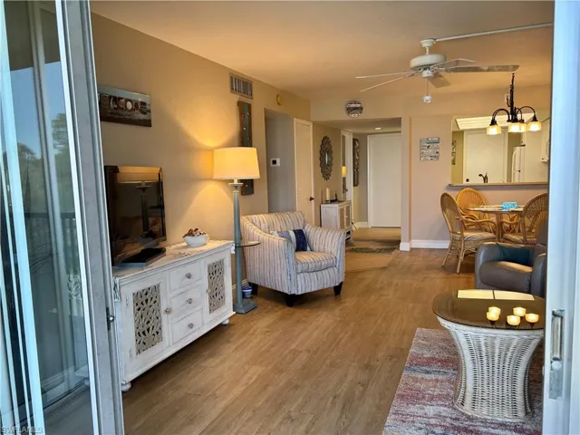 Living area with ceiling fan with notable chandelier, wood finished floors