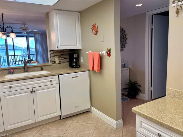 Kitchen with tasteful backsplash, light tile patterned floors, white cabinets, white dishwasher, and a sink