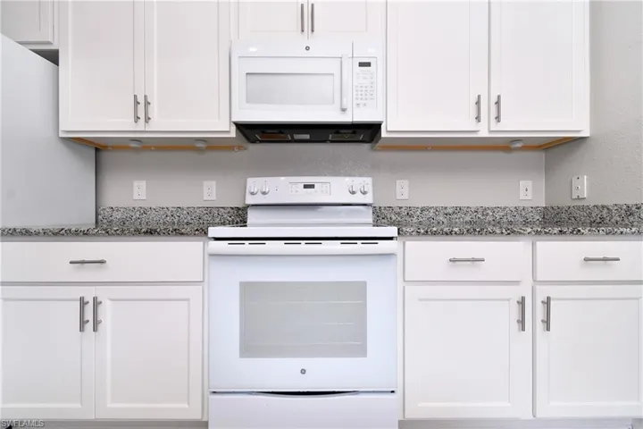 Kitchen featuring white appliances, white cabinetry, and light stone counters