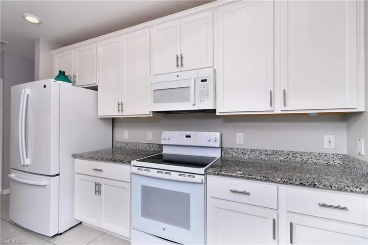 Kitchen with light tile patterned flooring, dark stone counters, white appliances, and white cabinetry