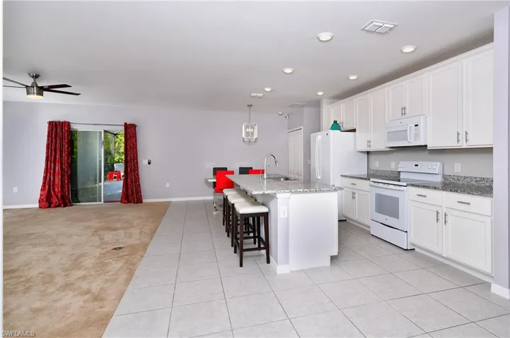 Kitchen with white appliances, ceiling fan, a center island with sink, sink, and light colored carpet