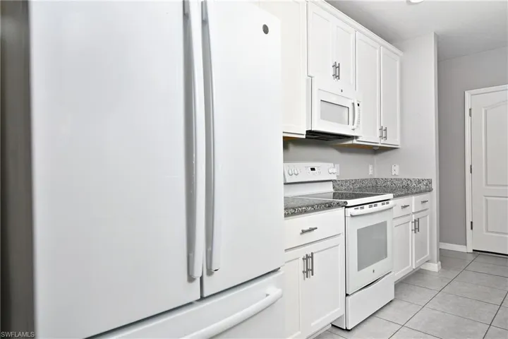 Kitchen featuring white appliances, white cabinetry, and light tile patterned flooring