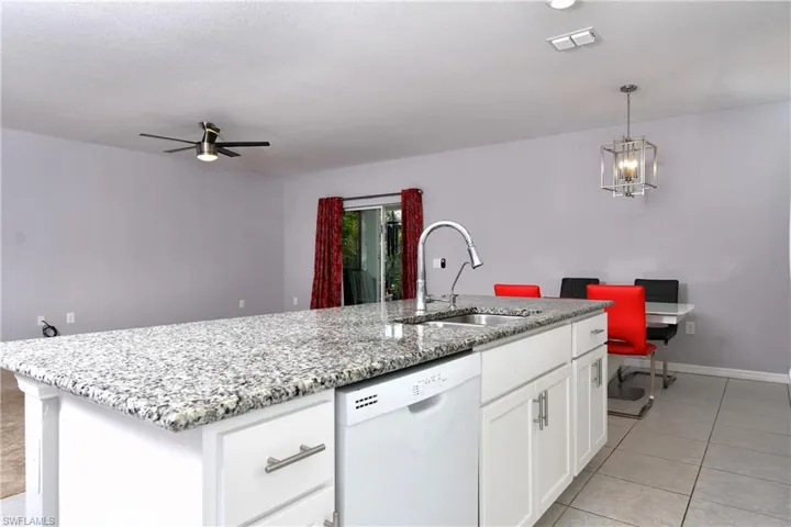 Kitchen with white cabinets, ceiling fan with notable chandelier, white dishwasher, a center island with sink, and sink