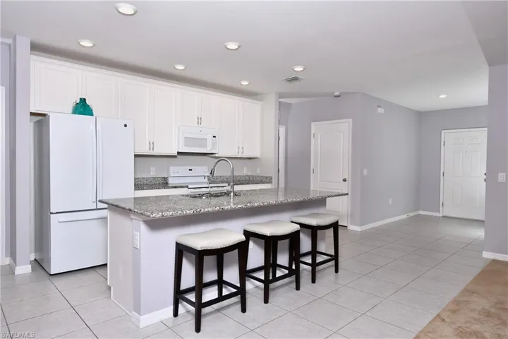 Kitchen featuring white appliances, a kitchen island with sink, dark stone countertops, and white cabinets
