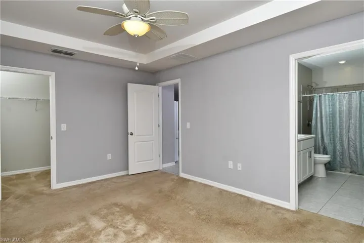 Unfurnished bedroom with connected bathroom, a closet, ceiling fan, a walk in closet, and light colored carpet