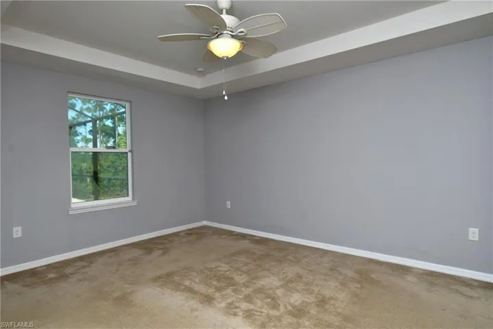 Carpeted spare room with a tray ceiling and ceiling fan
