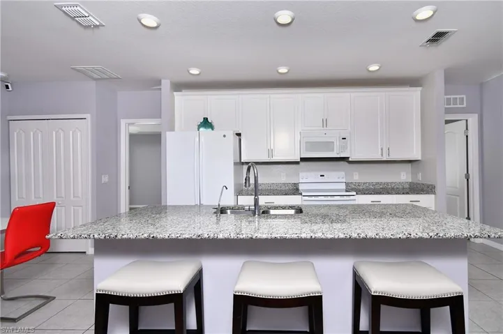Kitchen featuring white appliances, sink, an island with sink, and white cabinets