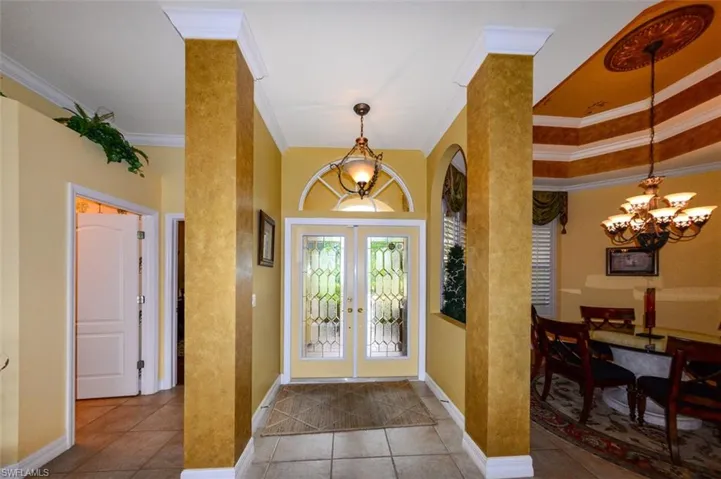 Tiled foyer featuring decorative columns, a chandelier, french doors, and crown molding