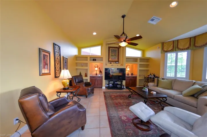 Living room featuring built in shelves, tile patterned floors, ceiling fan, and high vaulted ceiling