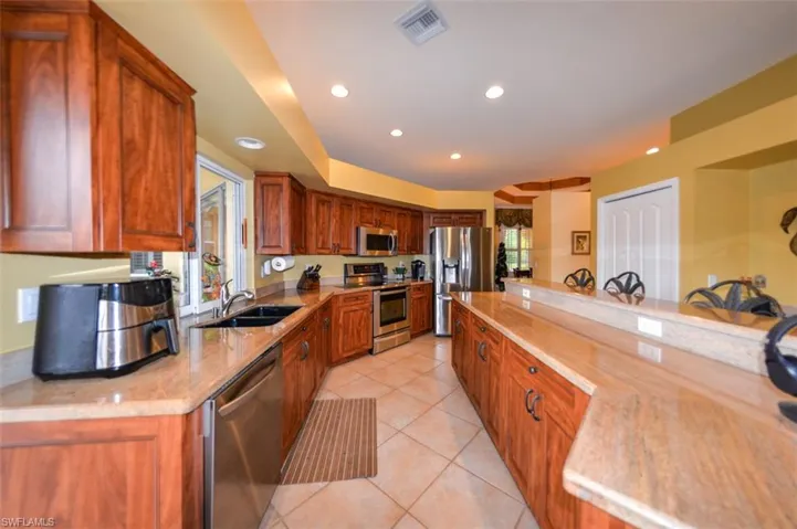 Kitchen with appliances with stainless steel finishes, light tile patterned floors, sink, and light stone countertops