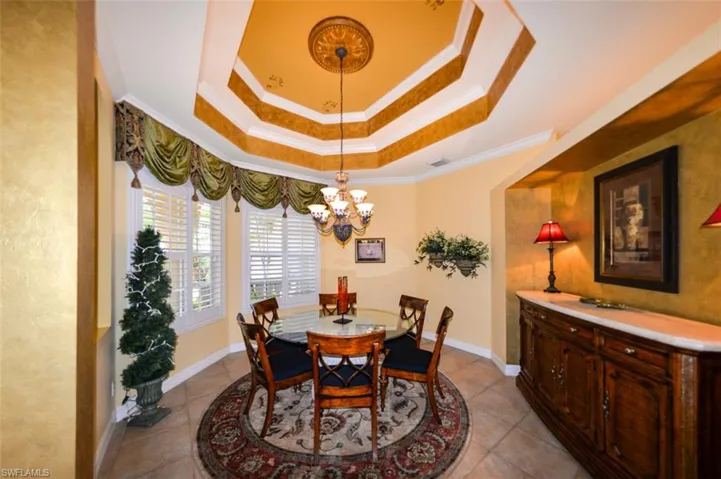 Dining area with tile patterned flooring, an inviting chandelier, a raised ceiling, and ornamental molding