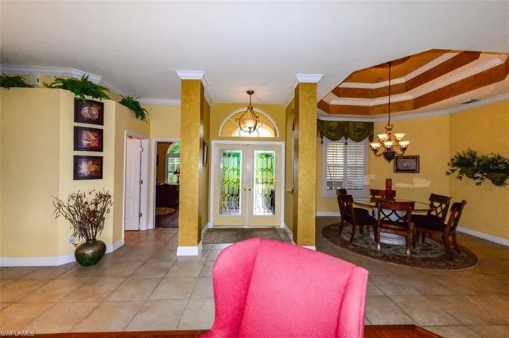 Tiled entryway featuring ornamental molding, an inviting chandelier, french doors, and a tray ceiling