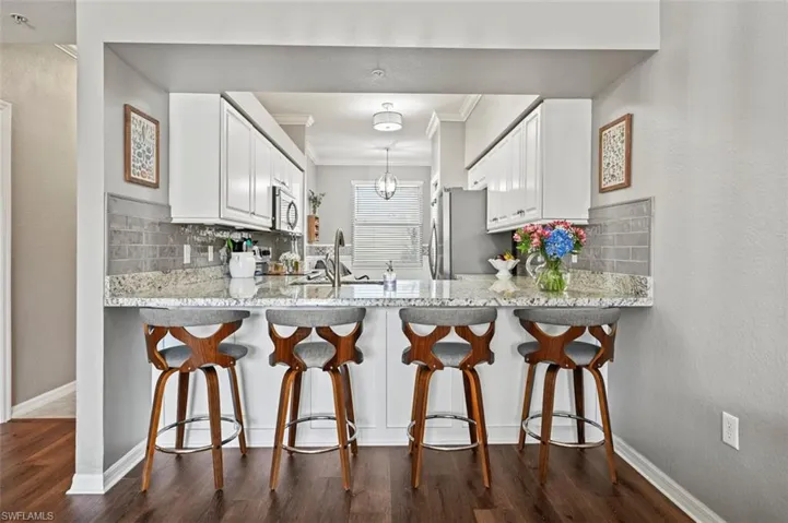 Kitchen featuring kitchen peninsula, decorative backsplash, white cabinets, and dark wood-type flooring