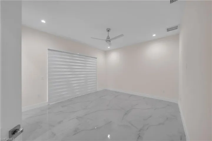 Empty room with baseboards, marble finish floor, visible vents, and a ceiling fan