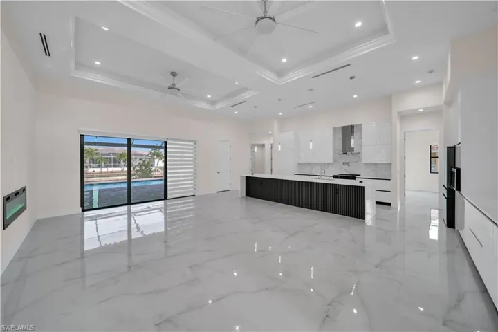 Kitchen with marble finish floor, a raised ceiling, a ceiling fan, modern cabinets, and wall chimney range hood