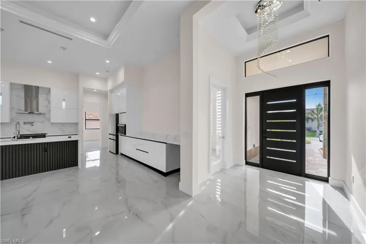 Entrance foyer featuring marble finish floor, a tray ceiling, recessed lighting, and a notable chandelier