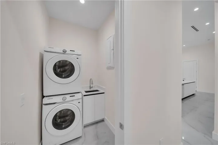 Laundry room with a sink, stacked washing maching and dryer, marble finish floor, visible vents, and recessed lighting