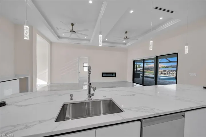 Kitchen featuring a sink, a raised ceiling, light stone countertops, open floor plan, and visible vents