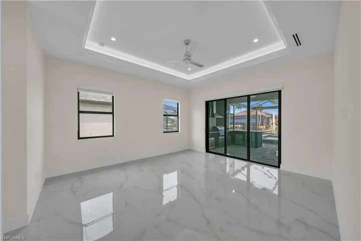 Unfurnished room featuring marble finish floor, a ceiling fan, a tray ceiling, and baseboards