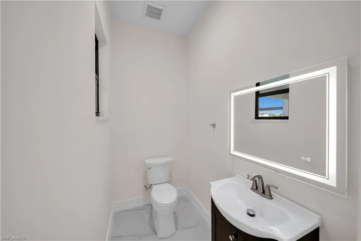 Bathroom with toilet, vanity, marble finish floor, baseboards, and visible vents