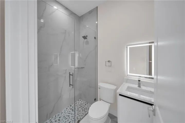 Bathroom with toilet, vanity, and a marble finish shower
