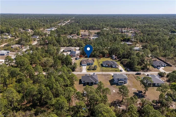 Aerial view of property and surrounding area featuring nearby suburban area and a heavily wooded area