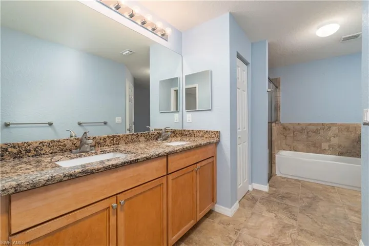 Full bath with a textured wall, double vanity, a bath, and a textured ceiling