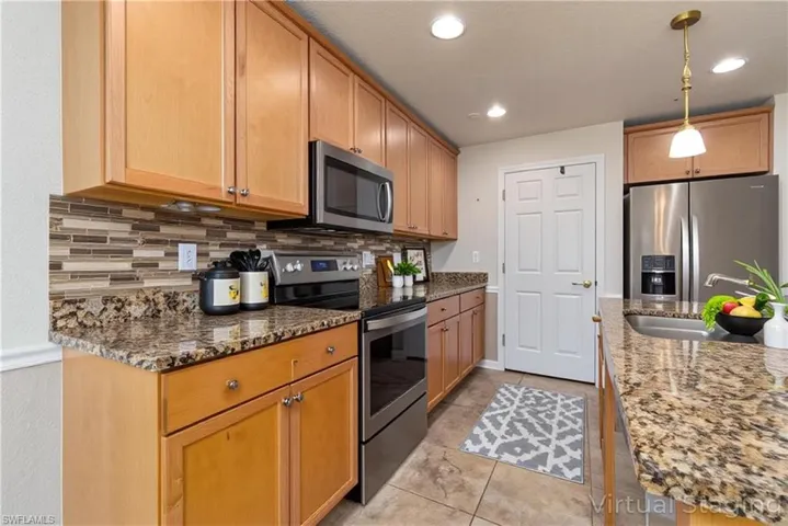 Kitchen with stainless steel appliances, hanging light fixtures, dark stone countertops, and tasteful backsplash (Digitally Staged)