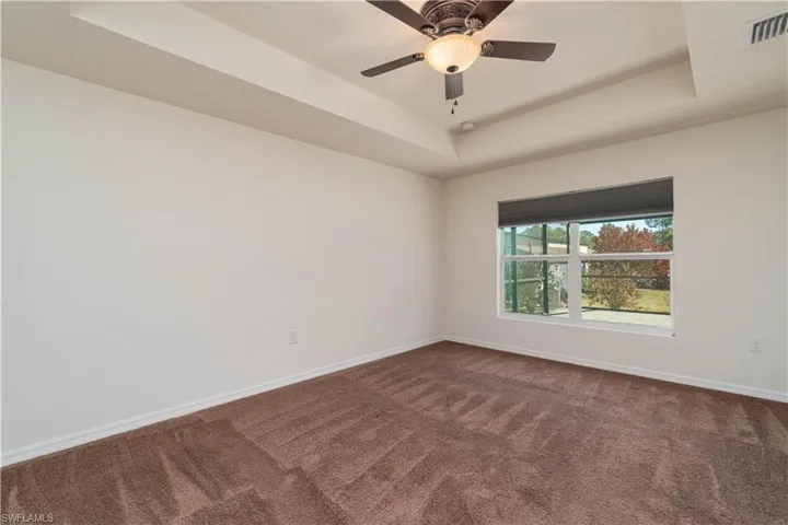 Spare room featuring a raised ceiling, dark carpet, and ceiling fan