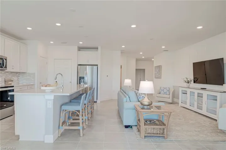 Kitchen featuring an island with double stainless sink, white cabinets, stainless steel appliances, open floor plan, and a kitchen bar