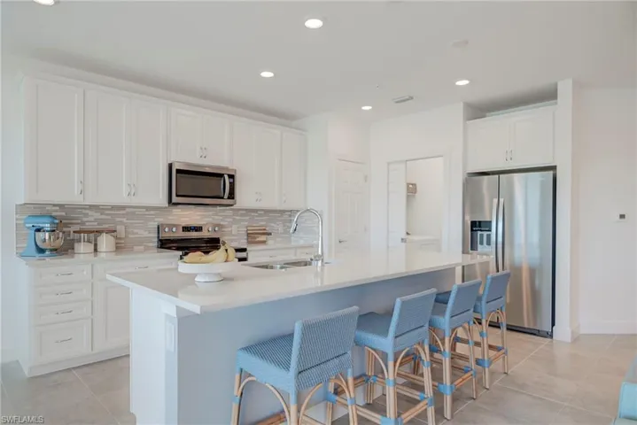 Kitchen with stainless steel appliances, recessed lighting, a kitchen breakfast bar, white cabinets, and a kitchen island with sink