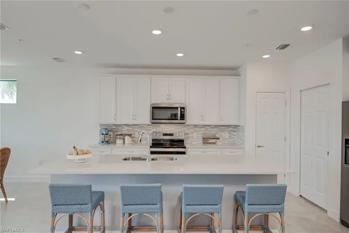 Kitchen featuring a quartz counters, tiled backsplash, & stainless steel appliances, white cabinetry
