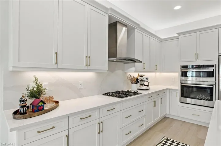 Kitchen featuring white shaker cabinetry, quartz countertops, a central island with a waterfall edge, stainless steel appliances, and wood-finish flooring