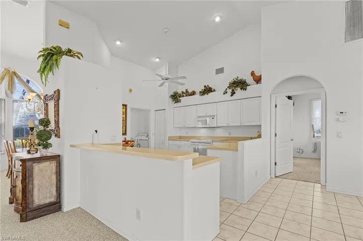 Kitchen with kitchen peninsula, white appliances, ceiling fan, high vaulted ceiling, and white cabinets