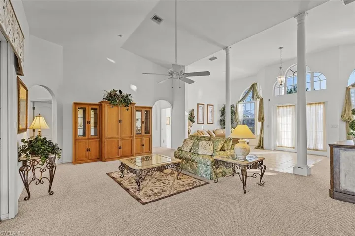 Living room with ceiling fan, light colored carpet, and a towering ceiling