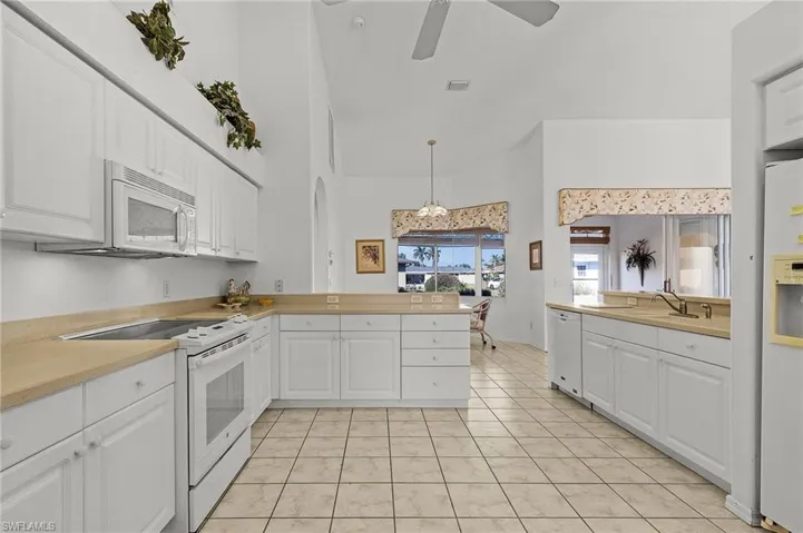 Kitchen with white appliances, white cabinets, hanging light fixtures, light tile patterned floors, and kitchen peninsula