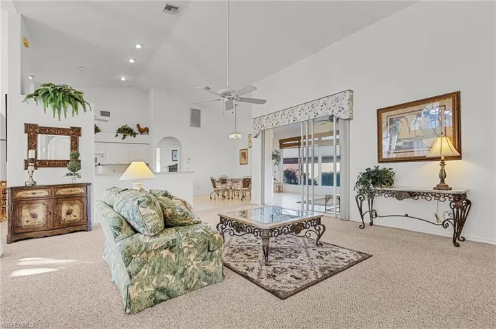 Carpeted living room featuring ceiling fan and high vaulted ceiling