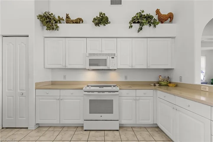 Kitchen with white cabinetry, white appliances, and light tile patterned floors