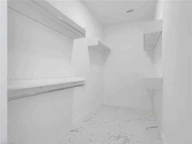 Walk-in closet featuring white walls, white-finish shelving, integrated hanging rods, white trim, and a marble-finish tile floor