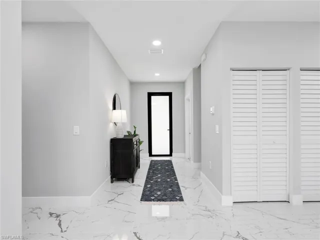 Hallway featuring white marble-look flooring, recessed ceiling lighting, a modern black-framed door, and white louvered closet doors
