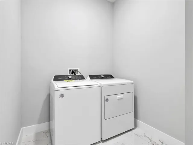 Dedicated laundry area featuring a white top-load washer, a white front-load dryer, light gray painted walls, a marble-look tile floor, and white baseboards