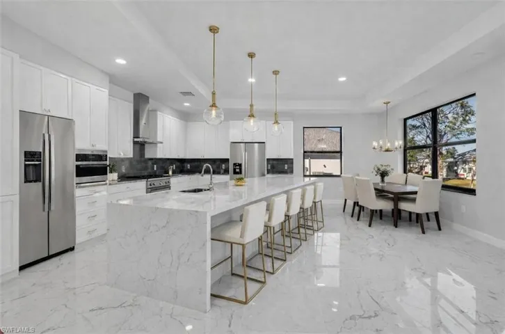 Kitchen featuring stainless steel appliances, white cabinets, a raised ceiling, light stone countertops, and a large island