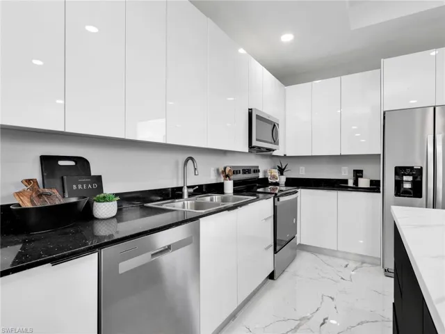 Modern kitchen featuring high-gloss white cabinetry, dark speckled countertops, stainless steel appliances, a double basin sink with a gooseneck faucet, and white marble-look flooring