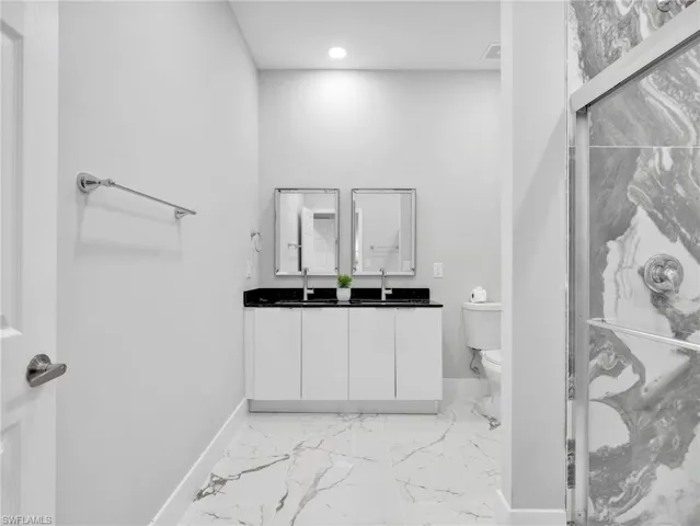 Double vanity with a black countertop and white cabinetry, complemented by a large format marble-look tile floor