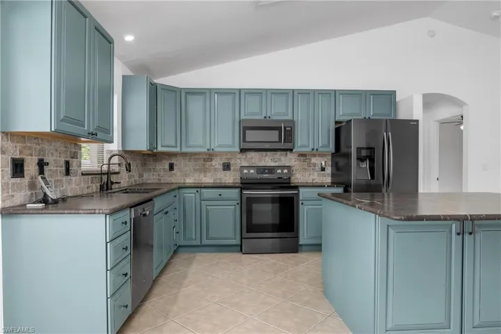 Kitchen featuring decorative backsplash, vaulted ceiling, light tile patterned floors, a sink, and stainless steel appliances