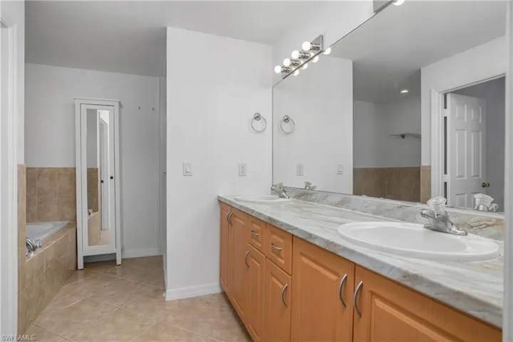 Full bathroom featuring double vanity, tiled bath, a sink, and tile patterned flooring