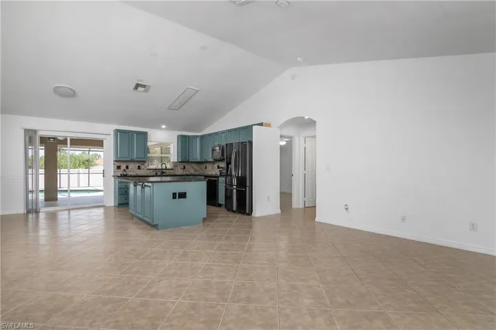 Kitchen featuring freestanding refrigerator, dark countertops, arched walkways, a sink, and blue cabinetry