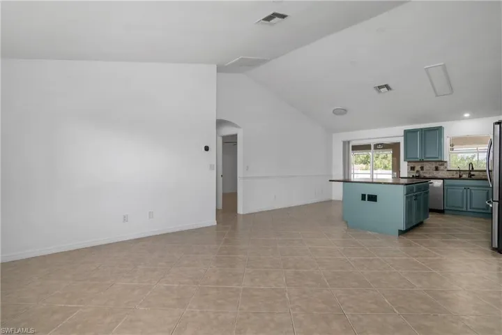 Kitchen with dark countertops, arched walkways, vaulted ceiling, tasteful backsplash, and visible vents